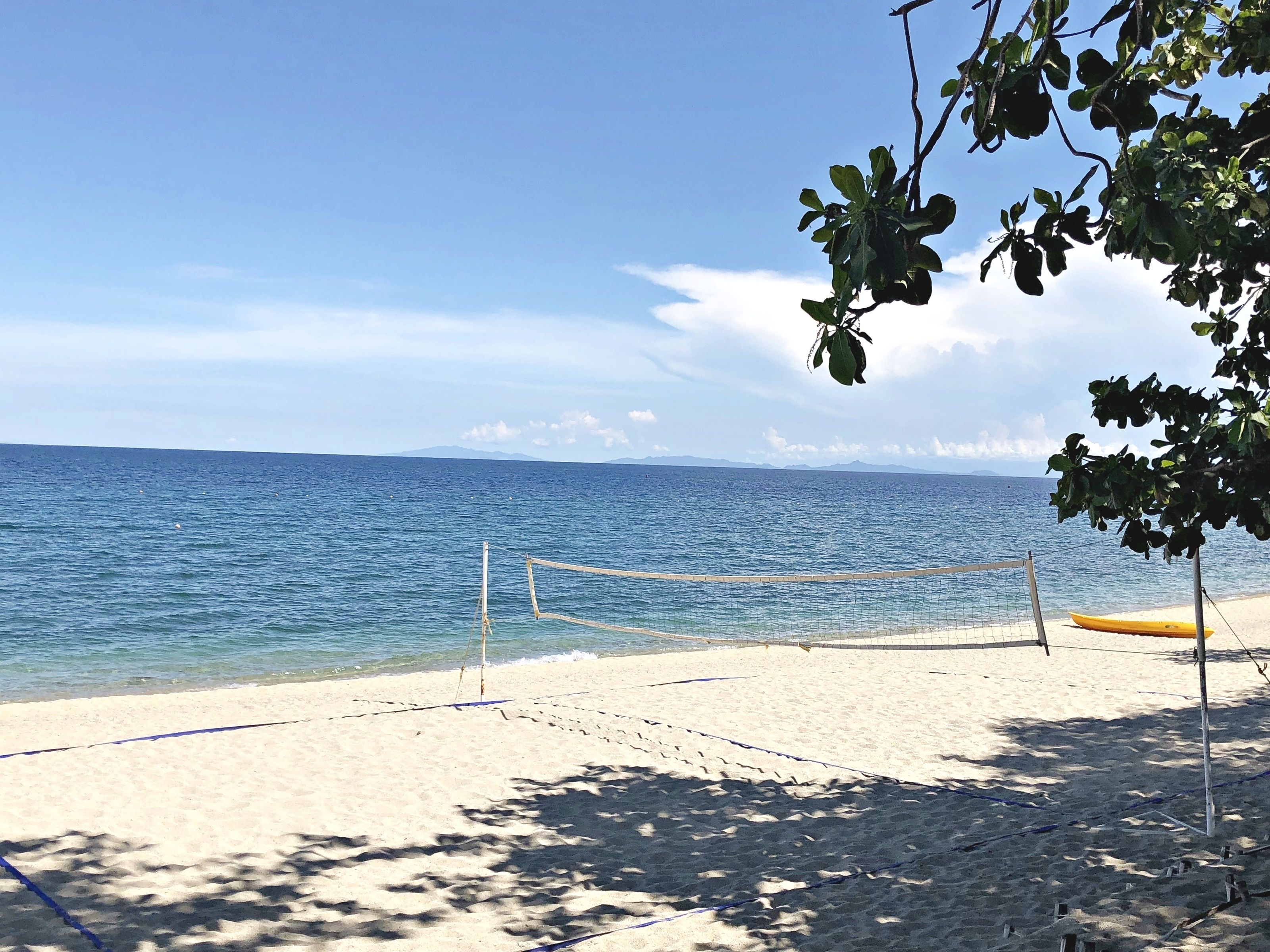 A beach with a volleyball net, a yellow kayak, and a clear view of the sea and distant mountains.