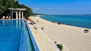Una playa con piscina, sillas de descanso y una zona de estar techada.