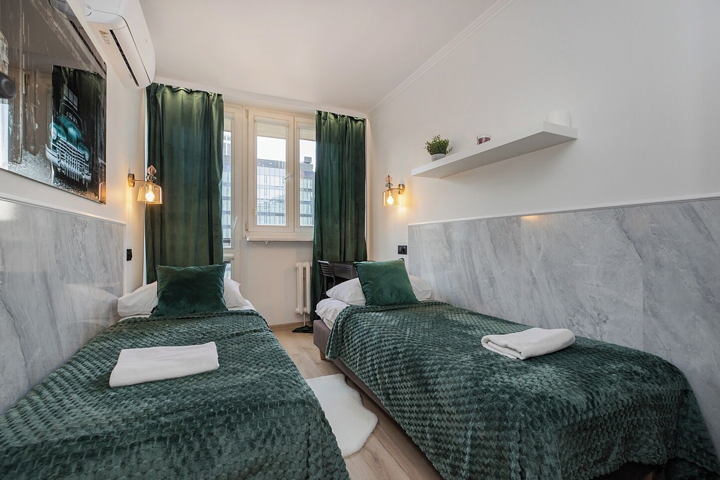 A hotel room with two beds, green curtains, a window, a radiator, and a shelf with a plant and a mug.