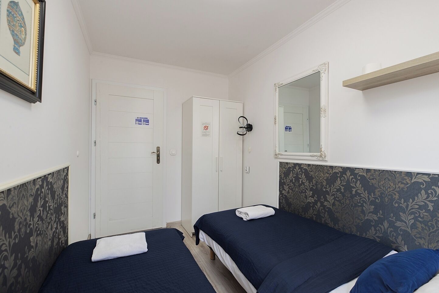 Ein Hotelzimmer mit zwei Betten, einem Spiegel, einer Tür und einem gerahmten Bild an der Wand.