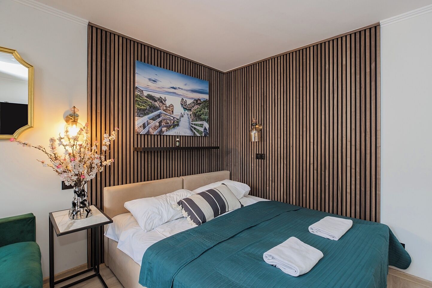 A hotel room with a bed, a nightstand with a vase of flowers, a wall-mounted picture, and a mirror.