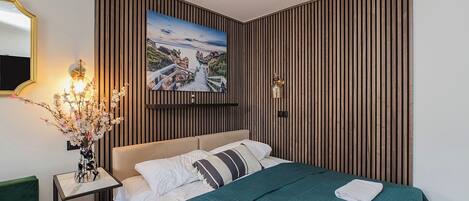 A hotel room with a bed, a nightstand with a vase of flowers, a wall-mounted picture, and a mirror.