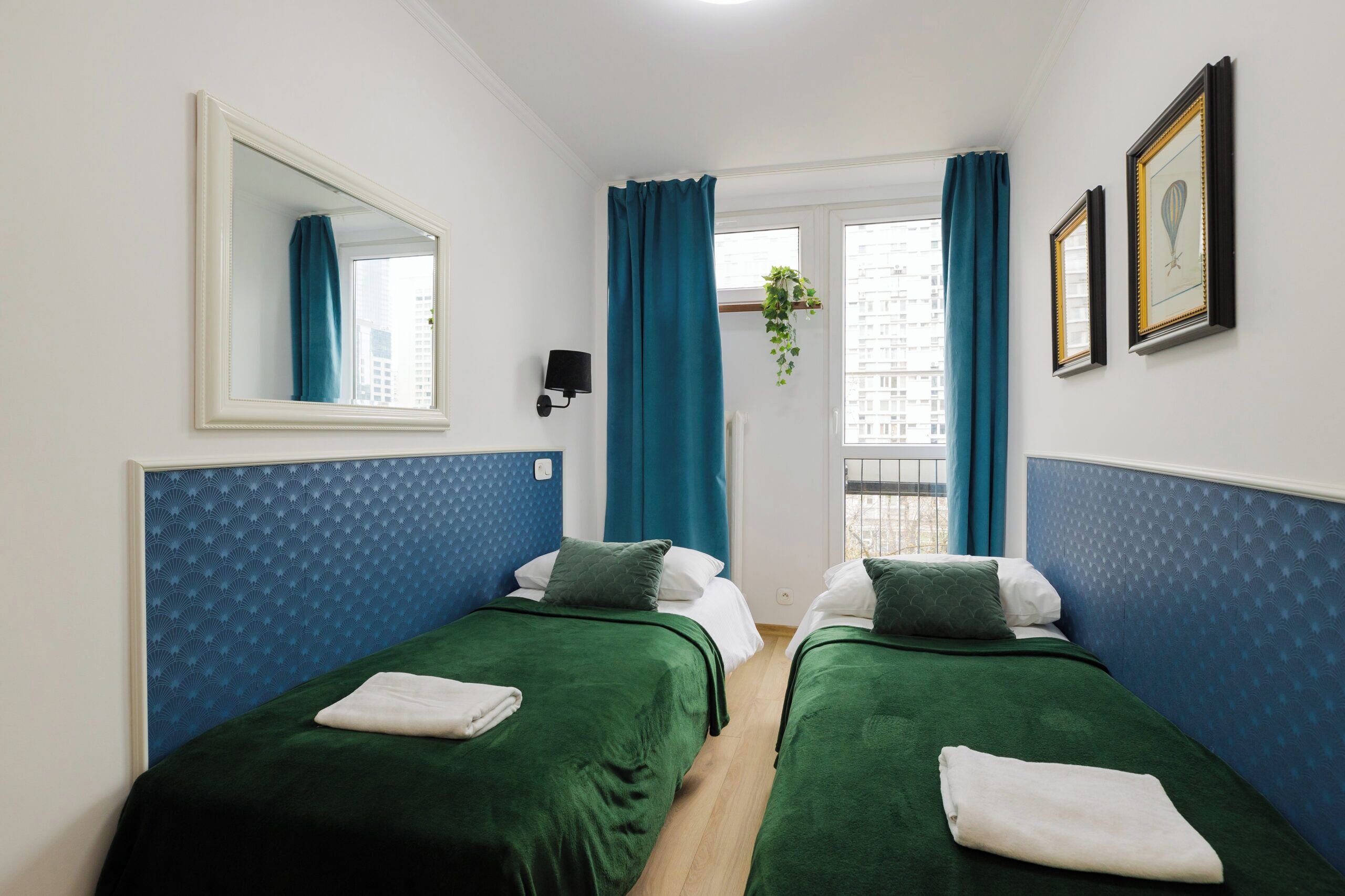 Ein Hotelzimmer mit zwei Betten, einem großen Spiegel, einem Fenster mit Vorhängen und einer Pflanze.