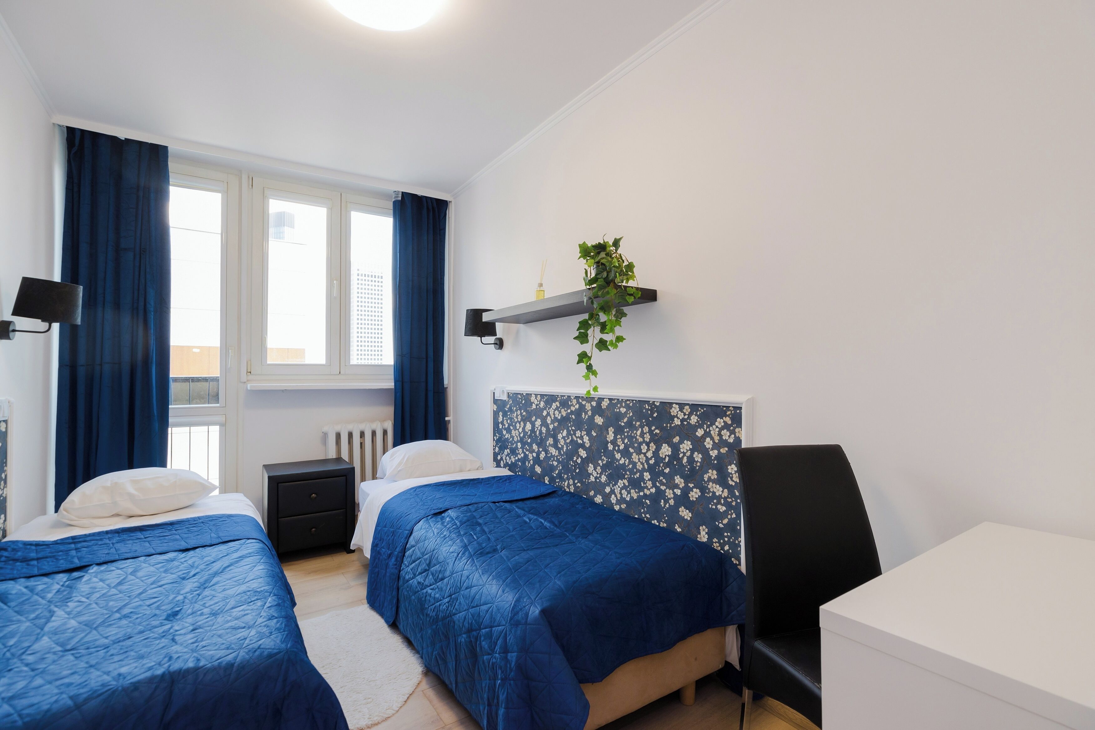 Une chambre avec deux lits, une table de chevet, une commode, un bureau et une fenêtre avec des rideaux.