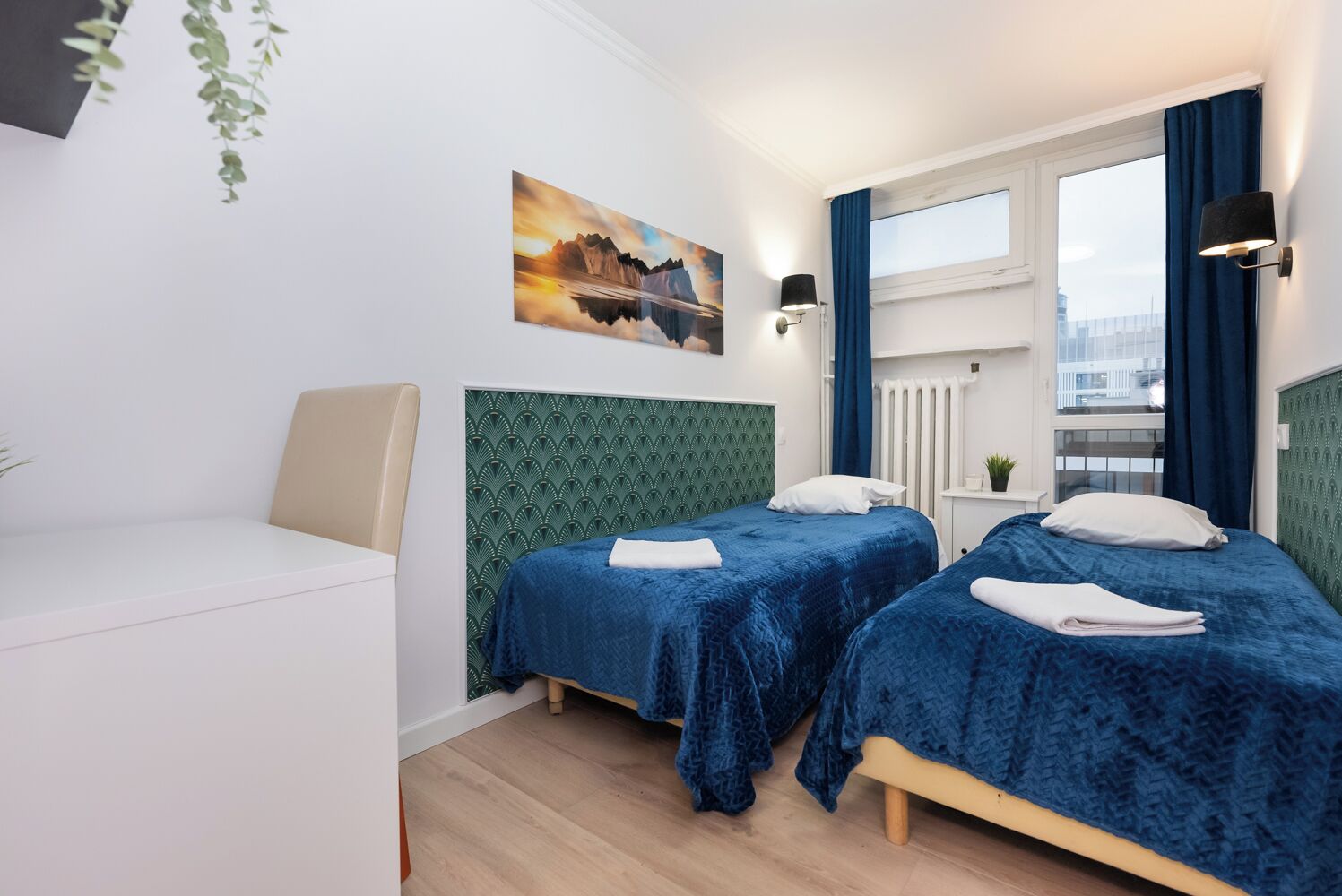 A hotel room with two beds, a sofa, a painting, a window with curtains, and a view of the city.