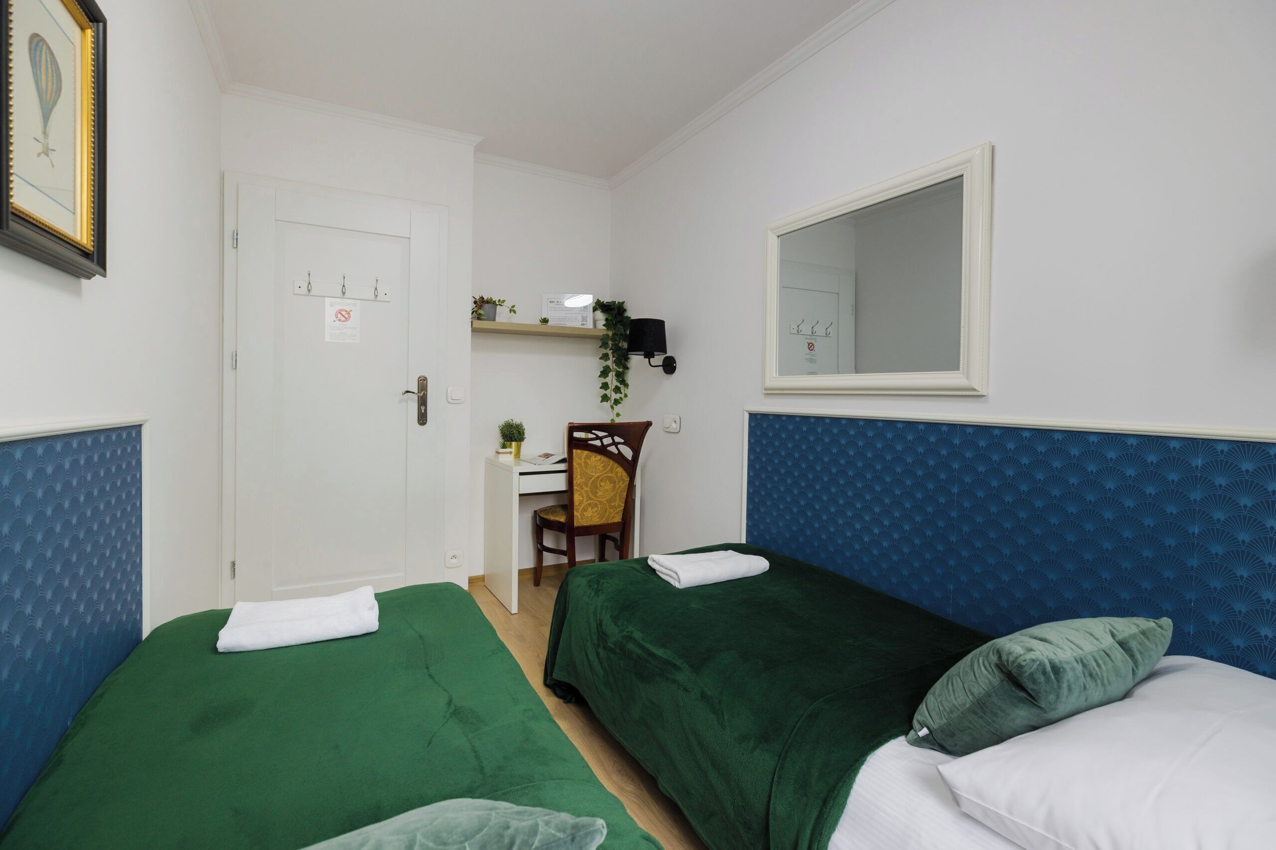 Ein Zimmer mit zwei Einzelbetten, einem Schreibtisch mit Stuhl, einem Spiegel und einer Tür mit einem Schild.