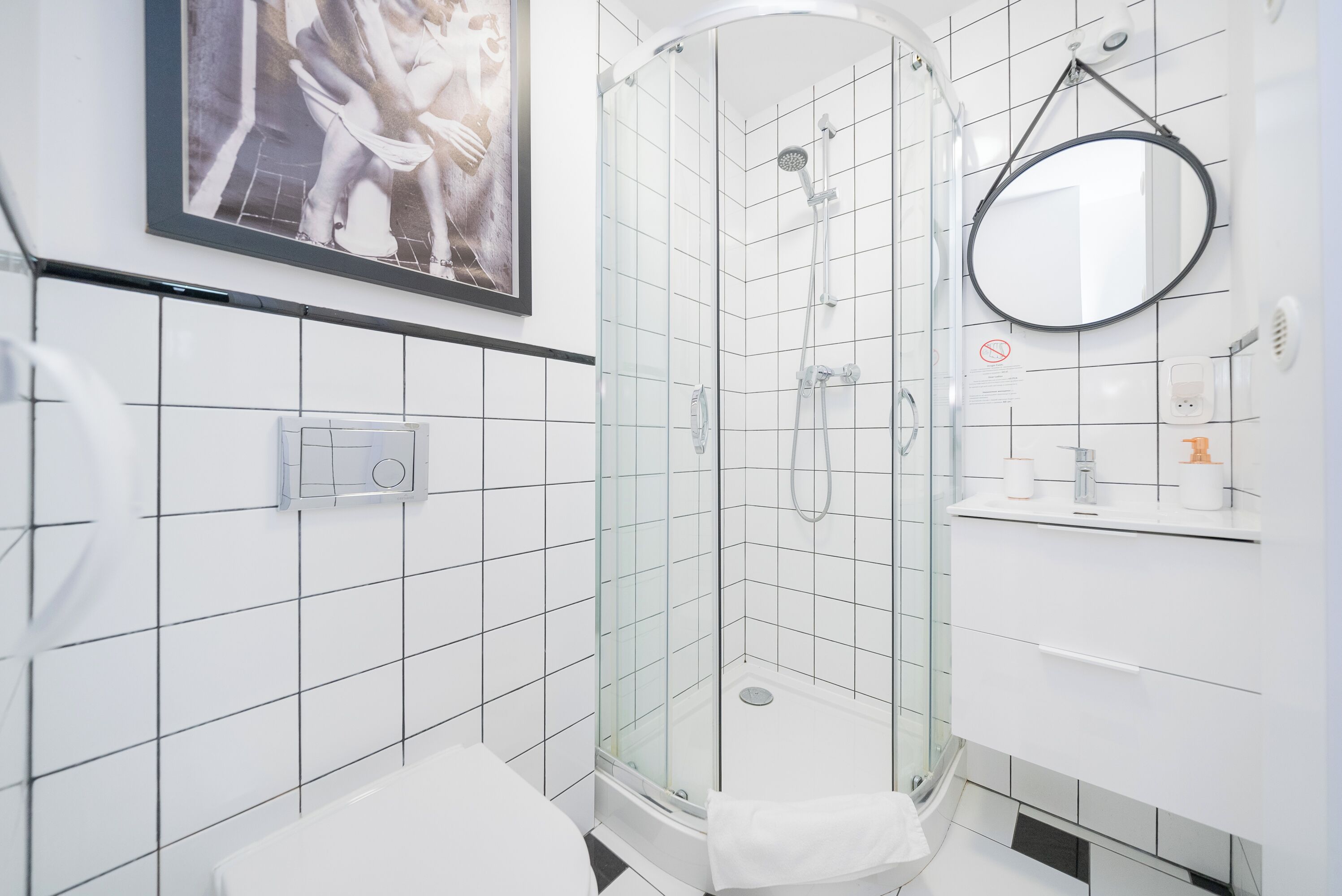 A modern bathroom with a glass-enclosed shower, a toilet, a sink with a mirror, and a framed picture on the wall.