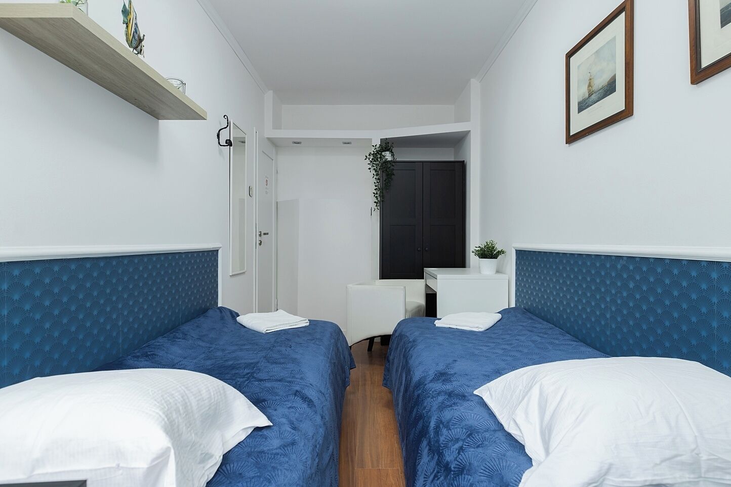 A room with two beds, a small desk, and a dark door.
