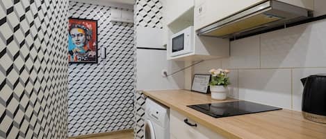 A modern kitchen with a microwave, stove, and a sink. There is a patterned wall and a framed picture on the wall.