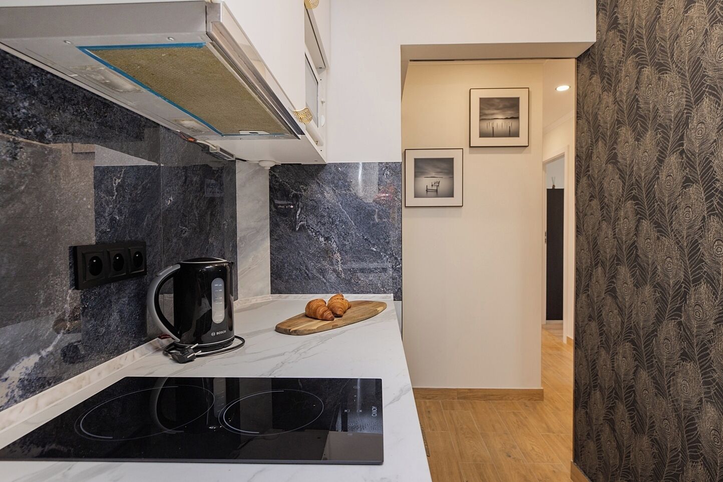 A modern kitchen with a black Bosch coffee maker, a wooden cutting board with croissants, and a marble backsplash.