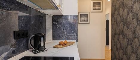 A modern kitchen with a black Bosch coffee maker, a wooden cutting board with croissants, and a marble backsplash.