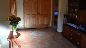 Una habitación con puerta de madera, suelo de baldosas, una mesita con un florero y un mueble con papeles.