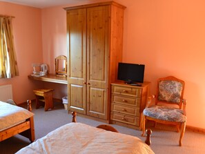 A bedroom with a bed, a wooden wardrobe, a desk with a chair, a television, and a patterned armchair.