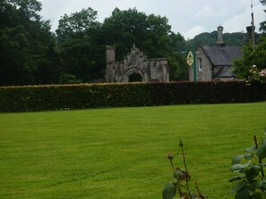 A historic stone building with a large archway, surrounded by a well-maintained lawn and dense trees.
