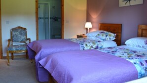 Un dormitorio con dos camas, una silla, una lámpara y una puerta que da al baño.
