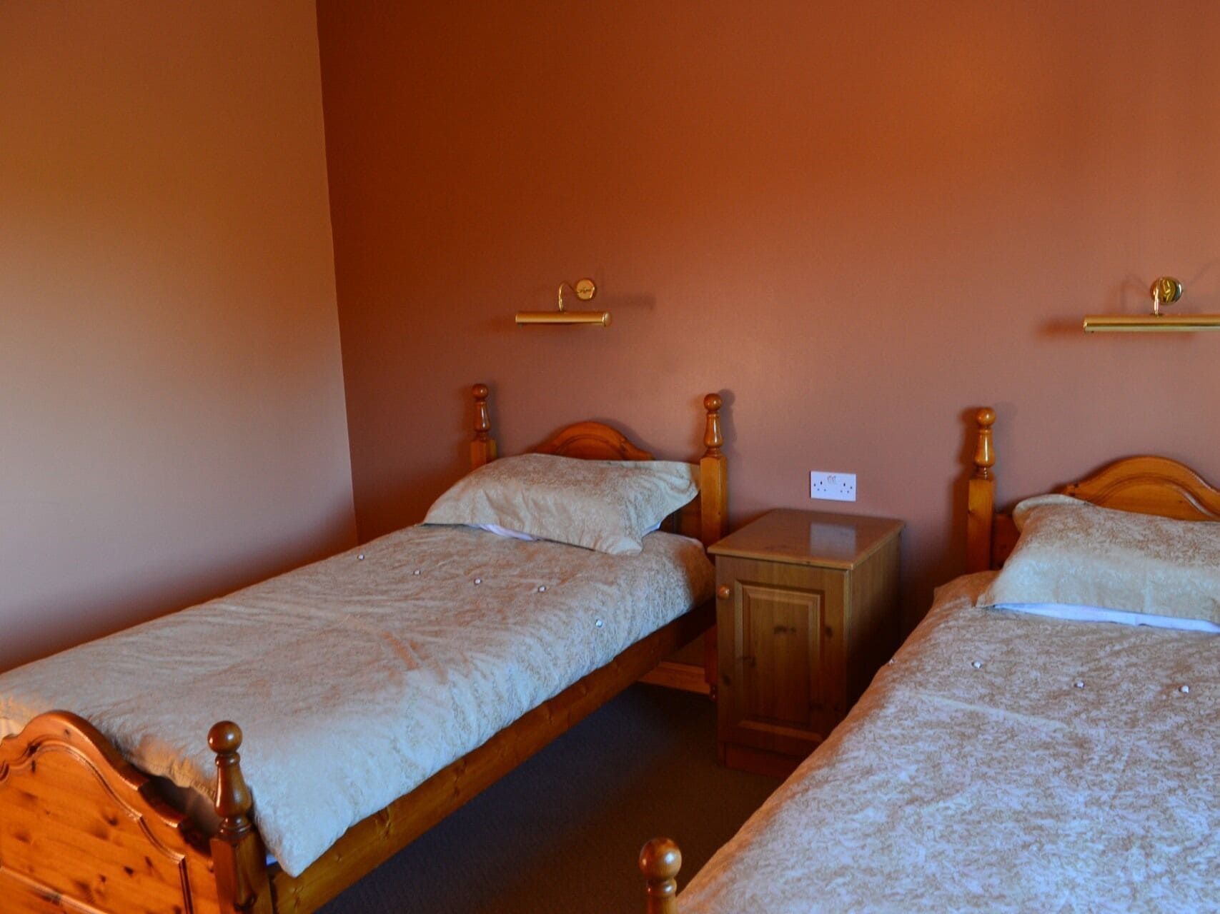 A room with two wooden beds, each with a wooden headboard and a small bedside table.