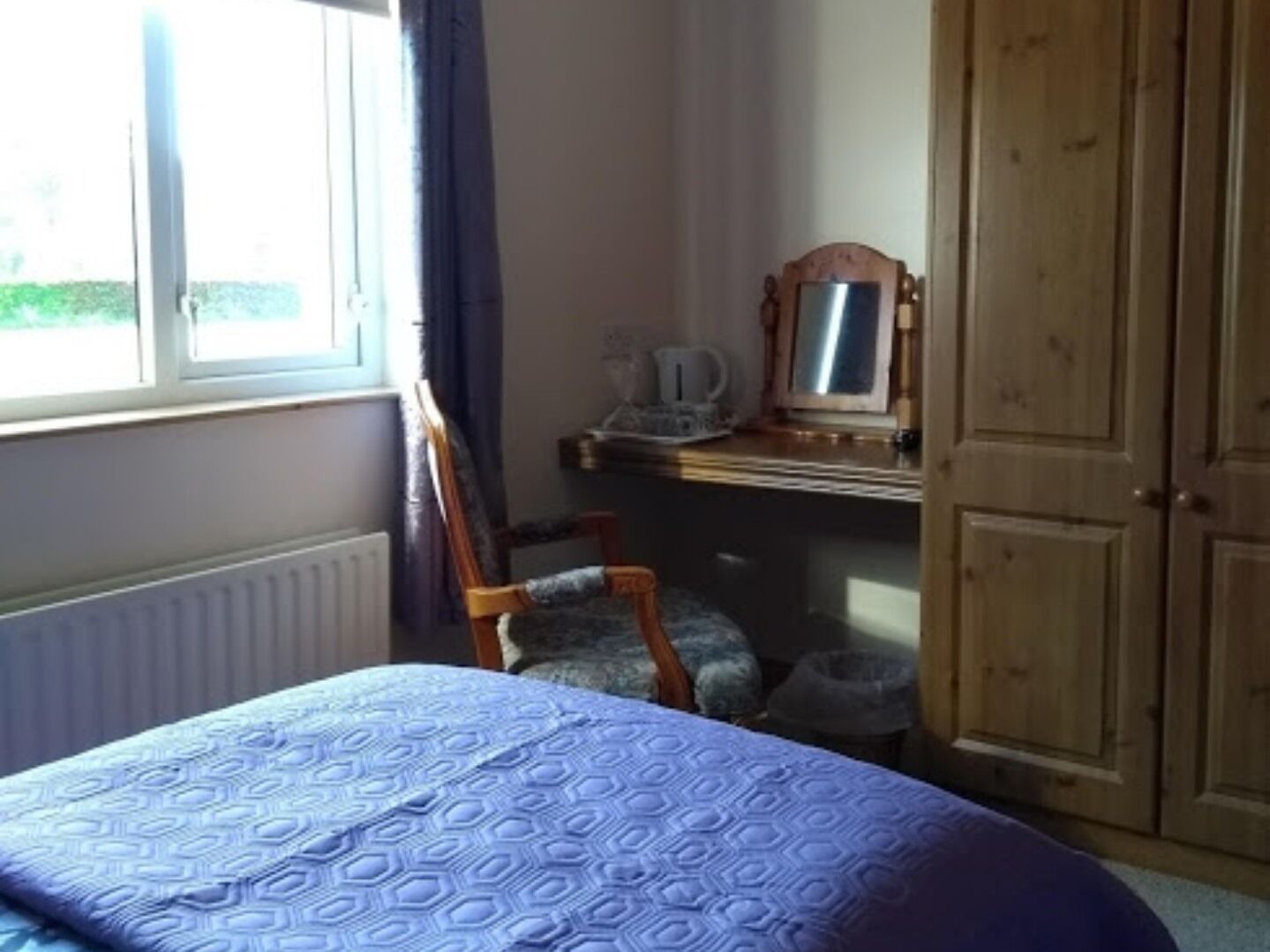 Een slaapkamer met een bed, een stoel, een dressoir en een spiegel.