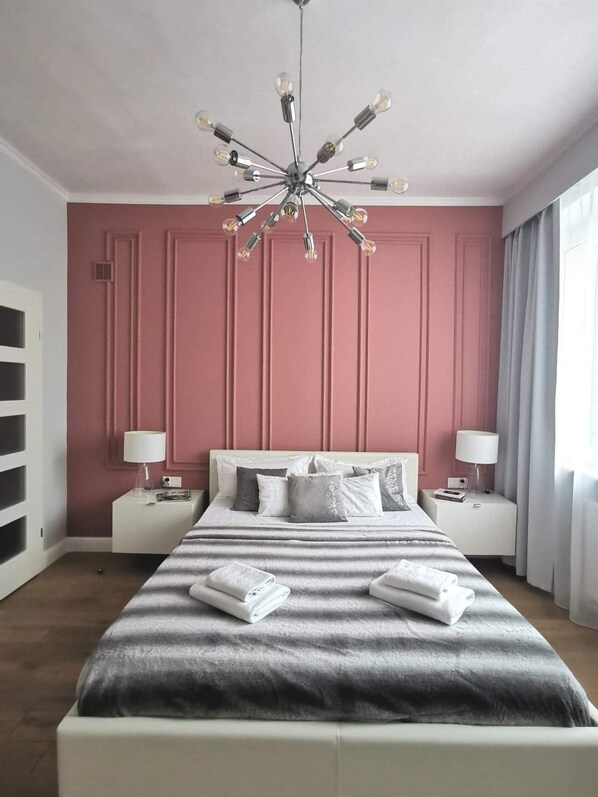 A bedroom with a large bed, two bedside tables, a modern chandelier, and a pink wall. - UNIT Centrum deLuX Plac Zbawiciela (Warsaw)