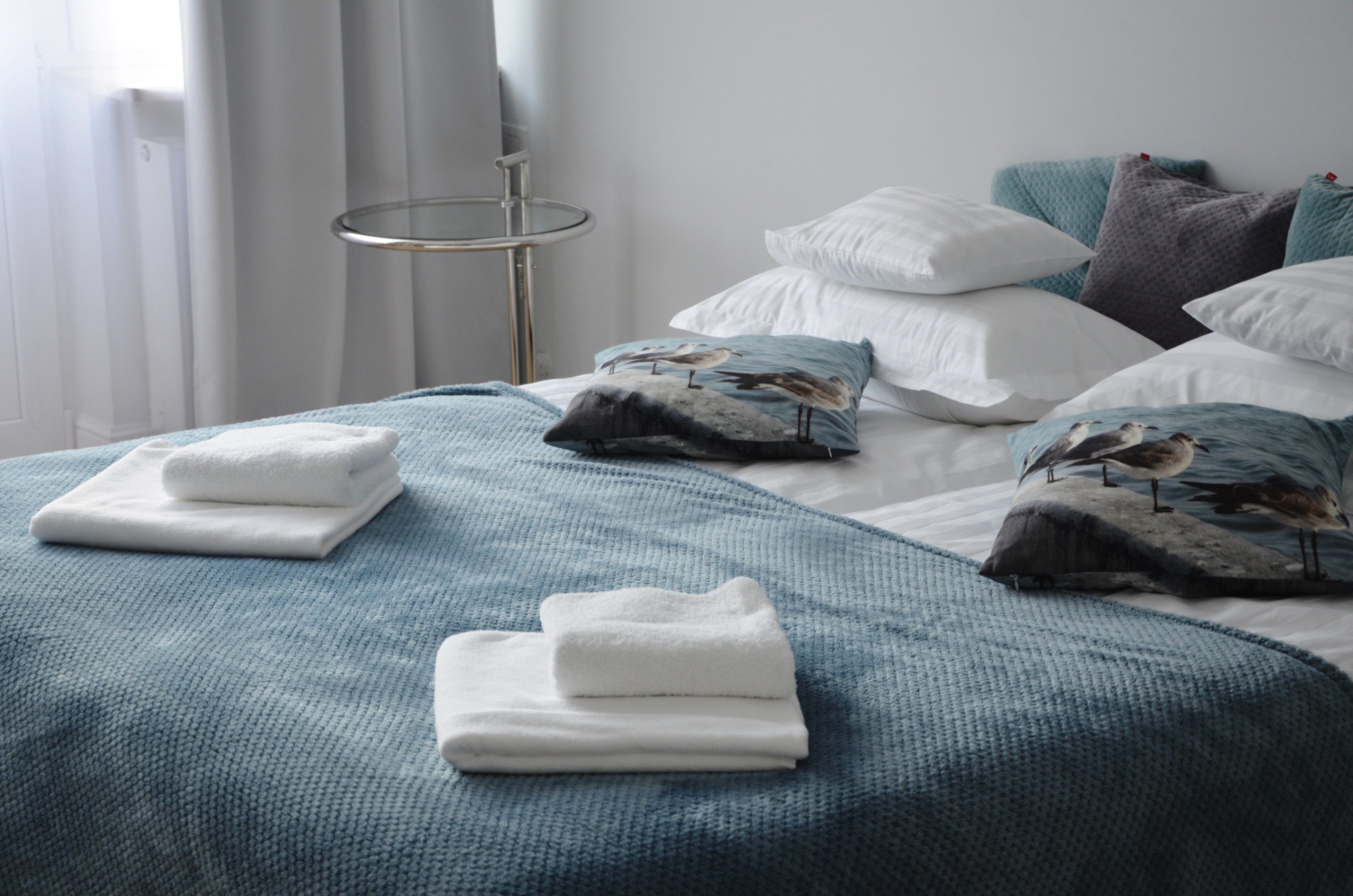 A neatly made bed with white and blue bedding, pillows with bird prints, and a folded white towel.