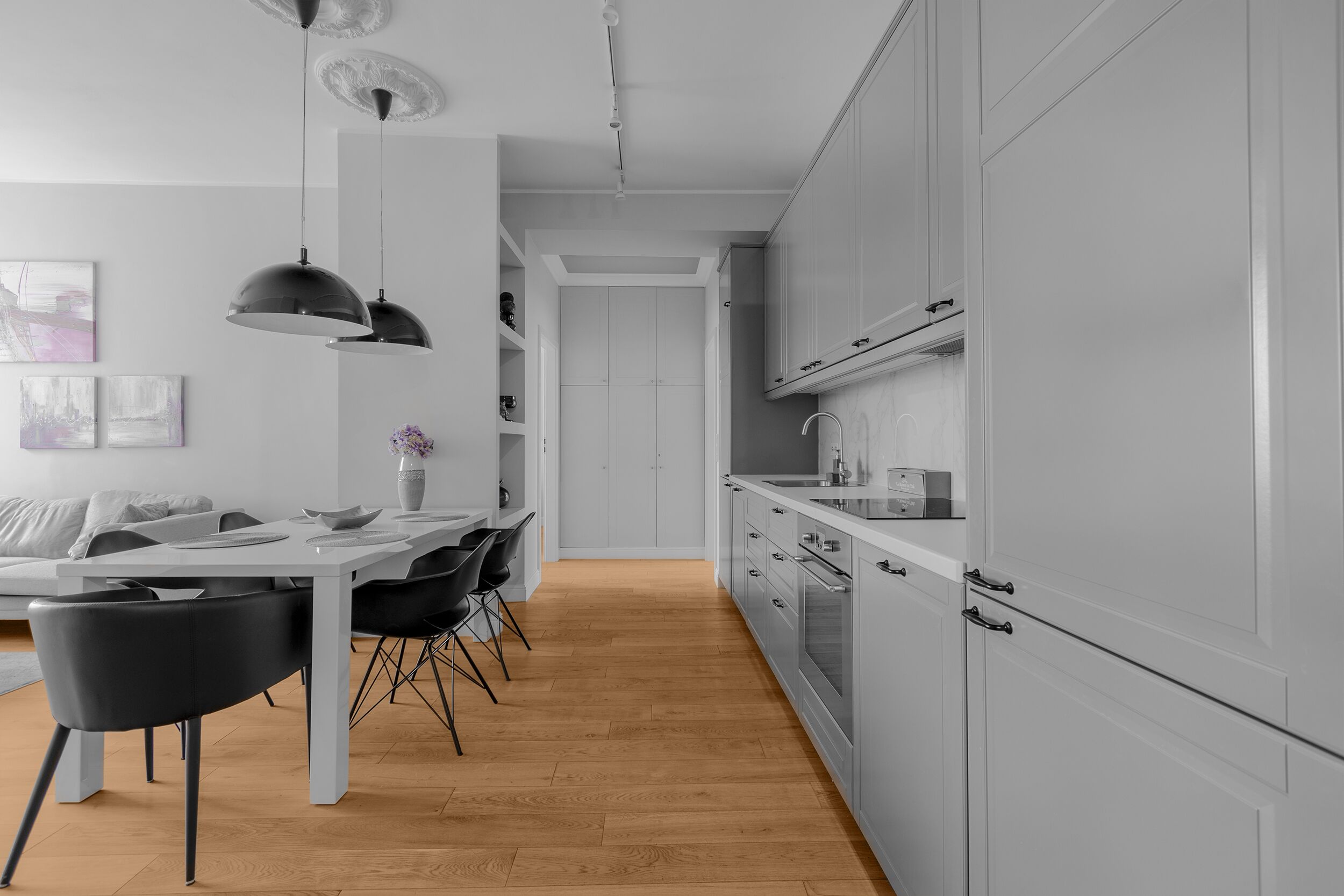 A modern kitchen with white cabinets, a wooden floor, and black chairs.
