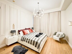 Un dormitorio moderno con una cama grande, una mesita de noche, una silla, una alfombra de piel y una araña.