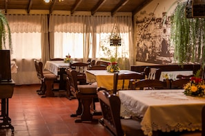 Un comedor con mesas y sillas de madera, manteles de encaje blanco y plantas colgantes.