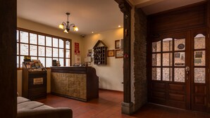 A reception area with a wooden reception desk, a bulletin board, and a stone wall. - Hotel Bella Casona (Riobamba)