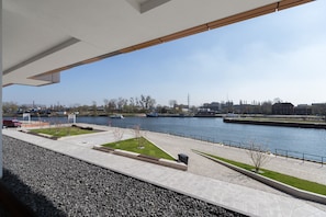 A riverside walkway with a clear view of the river, a bridge, and distant buildings. - Navy Group - Lion's Castle (Gdansk)
