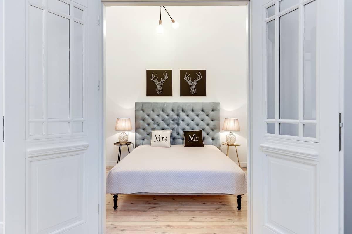 Quarto com cabeceira estofada, duas luminárias de mesa, cama com colcha acolchoada e duas peças de arte de veados montadas na parede.
