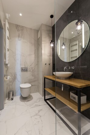 A modern bathroom with a marble floor, a white toilet, a wooden vanity with a sink, and a large mirror. - Navy Group - Lion's Castle (Gdansk)