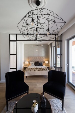 A modern bedroom with a geometric chandelier, a tufted headboard, and a large window. - Navy Group - Lion's Castle (Gdansk)