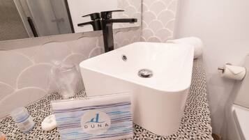 A bathroom with a white sink, a towel, a bottle, and a bag with the text "DUNA".