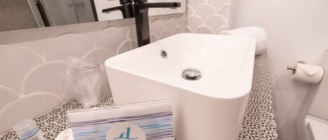 Un baño con un lavabo blanco, una toalla, una botella y un bolso con la inscripción "DUNA".