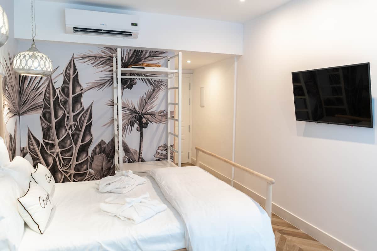 A bedroom with a bed, white bedding, a wardrobe with a leaf-patterned back, a hanging light fixture, and a mounted TV.