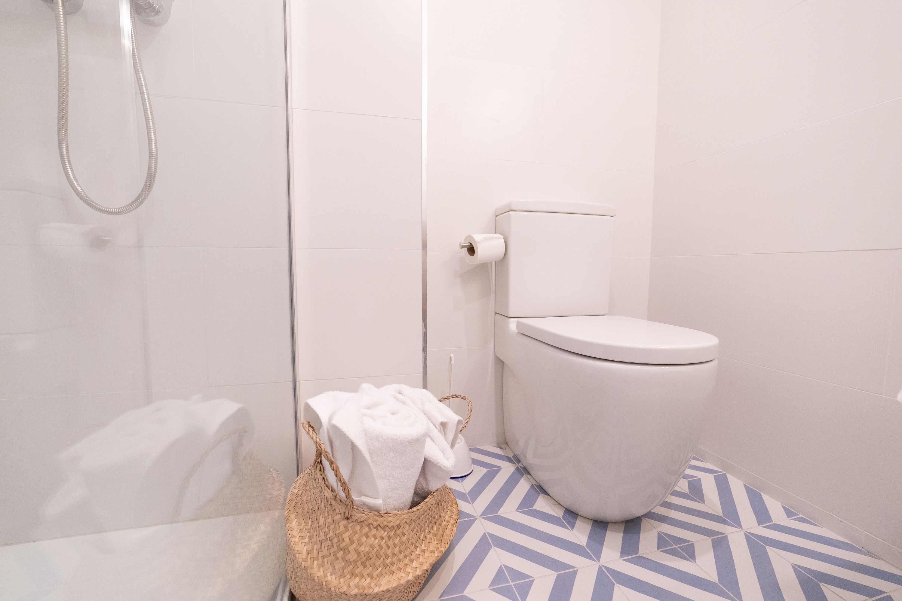 Ein Badezimmer mit Dusche, Toilette und einem gemusterten Boden.
