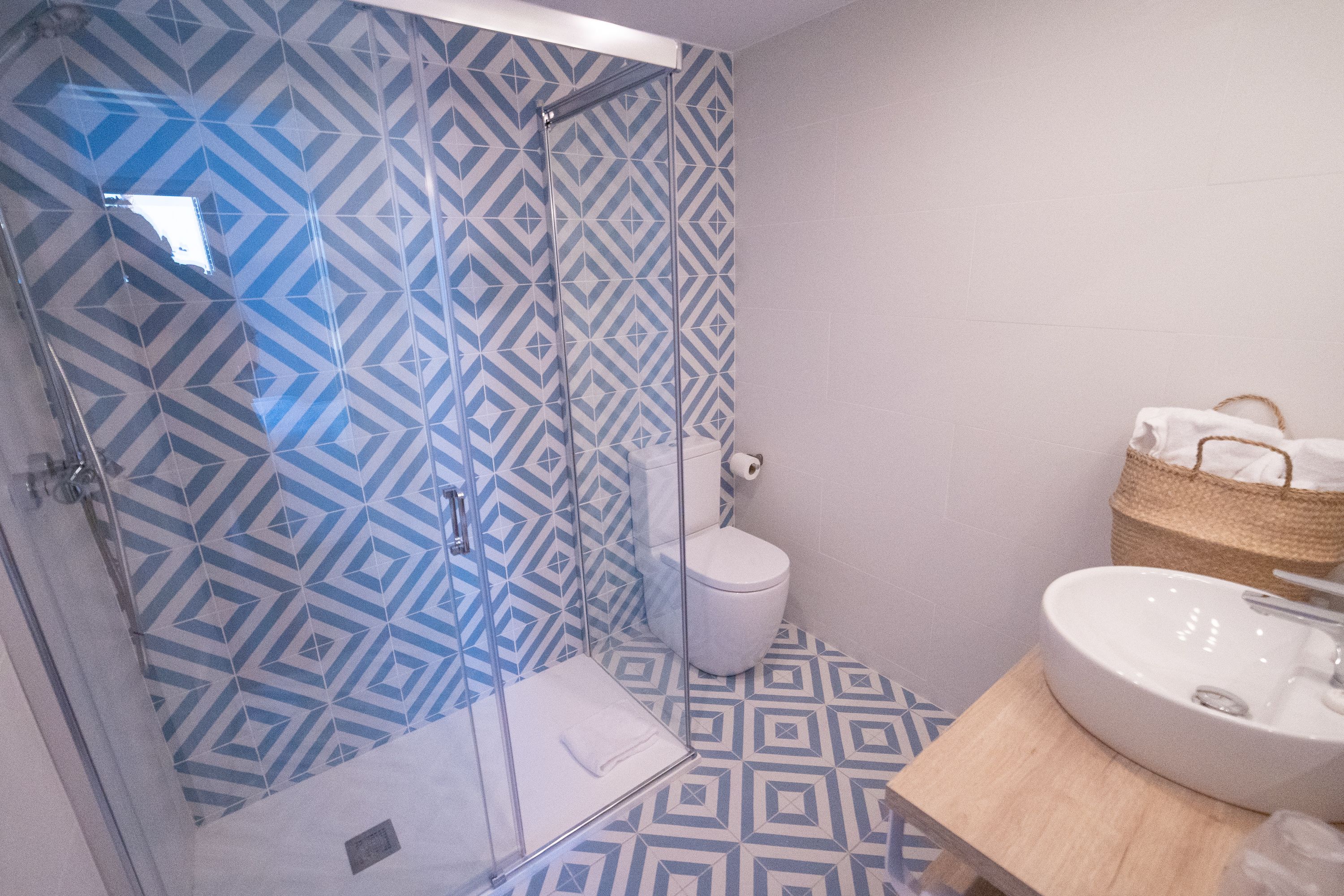 Ein Badezimmer mit einer Dusche, deren Wand ein geometrisches Muster aufweist, einer weißen Toilette und einem Waschbecken mit Holzauskleidung.