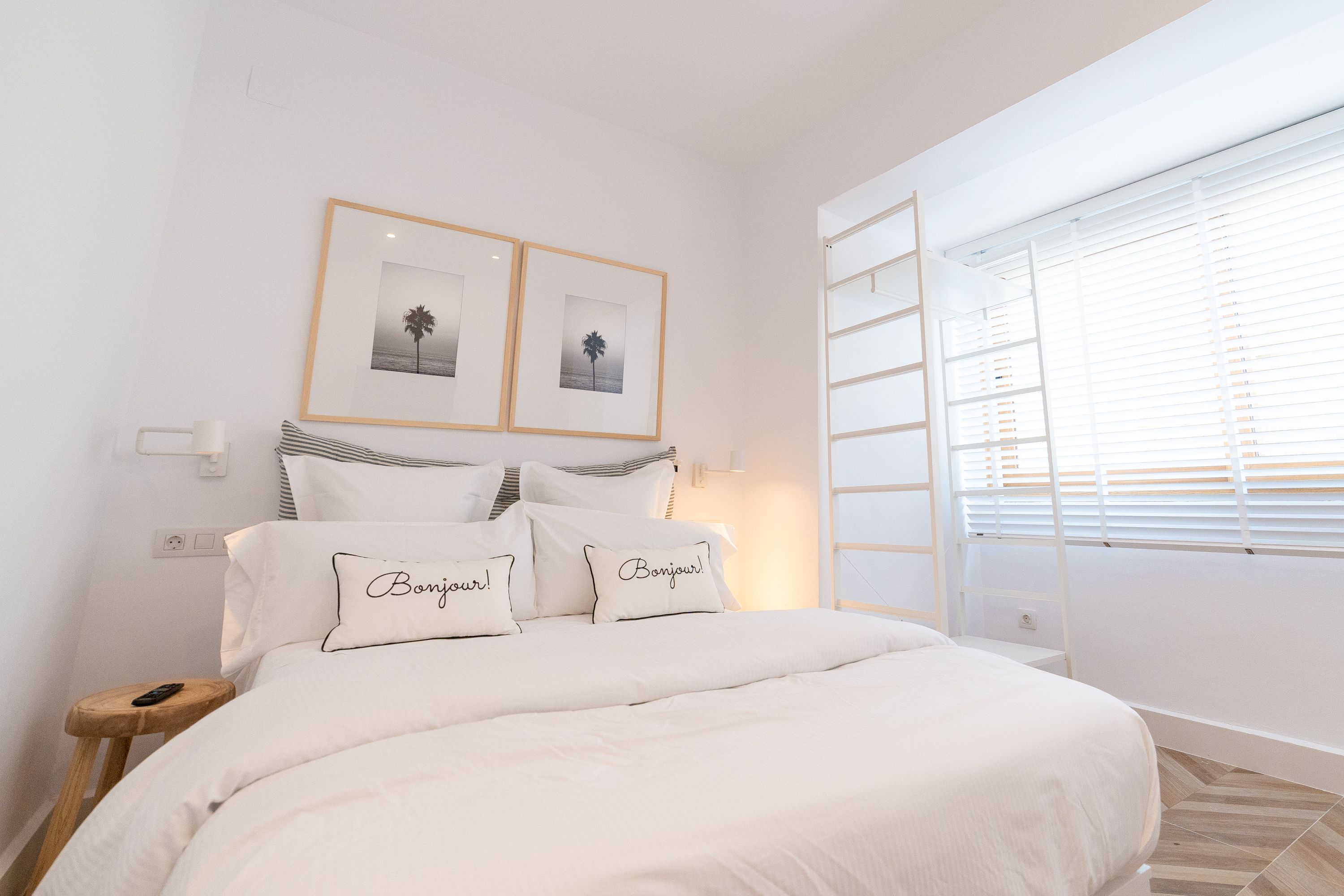 A bedroom with a bed, two framed pictures on the wall, and a window with blinds.