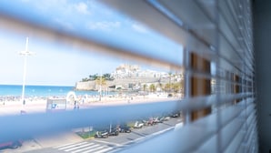 Vista costera con playa, scooters estacionados y un edificio histórico sobre una colina.