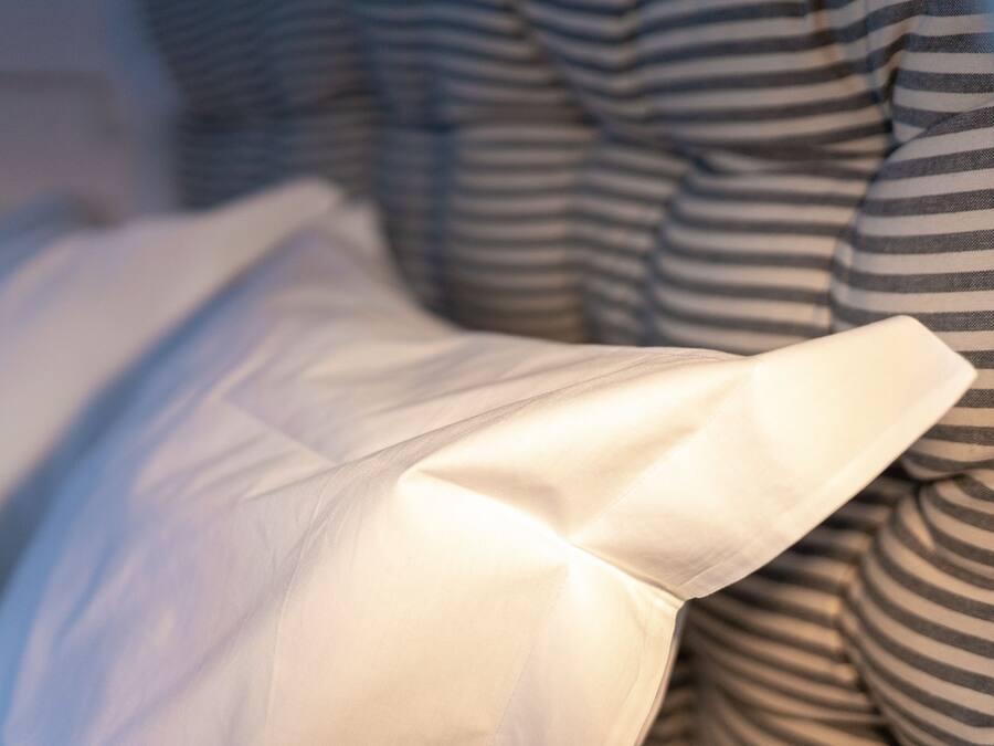 Primer plano de una cama con ropa de cama a rayas y una almohada blanca.
