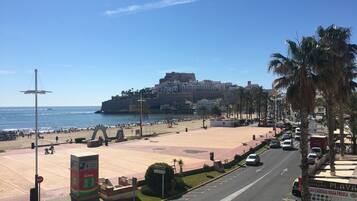 Un paisaje urbano costero con una fortaleza histórica, una playa y una calle concurrida.