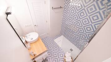 Une salle de bain avec un mur de douche orné d’un motif géométrique, une porte blanche, un meuble-lavabo en bois et des toilettes.