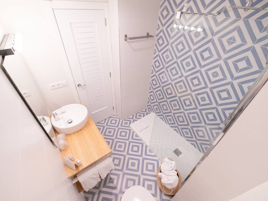 Une salle de bain avec un mur de douche orné d’un motif géométrique, une porte blanche, un meuble-lavabo en bois et des toilettes.