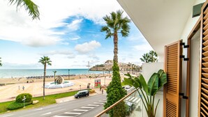 Un balcón con vista a una playa, palmeras y una carretera con vehículos.