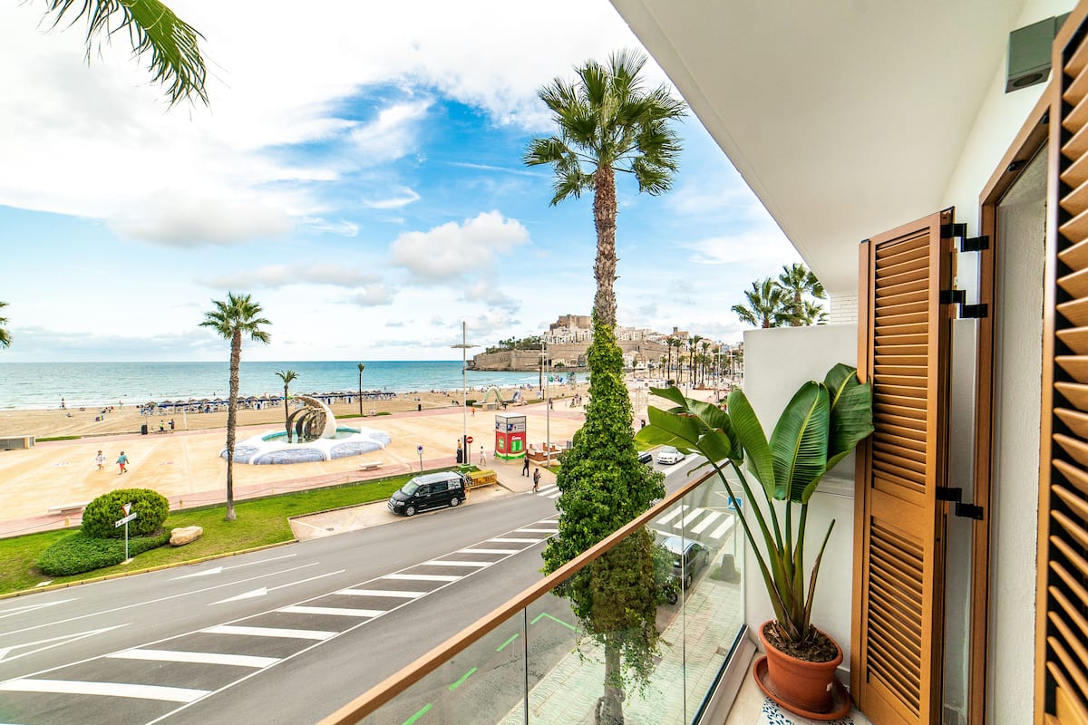 A balcony with a view of a beach, palm trees, and a road with vehicles.