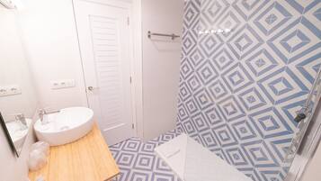 A bathroom with a white sink, wooden countertop, and a shower with a geometric tile pattern.
