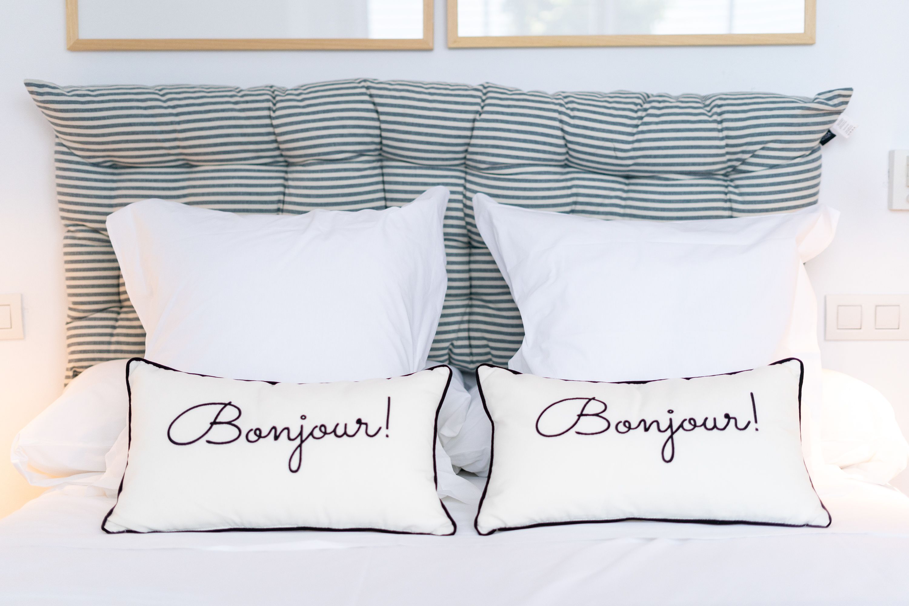 Una cama con almohadas a rayas y dos almohadas con la palabra "Bonjour!" escrita.