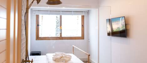 A bedroom with a bed, a window, a TV mounted on the wall, and a shower with a glass door.
