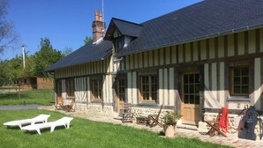 A traditional half-timbered house with a sloped roof, a stone foundation, and a well-maintained lawn with outdoor seating. - L'auberge du Mont (Le Breuil-en-Auge)