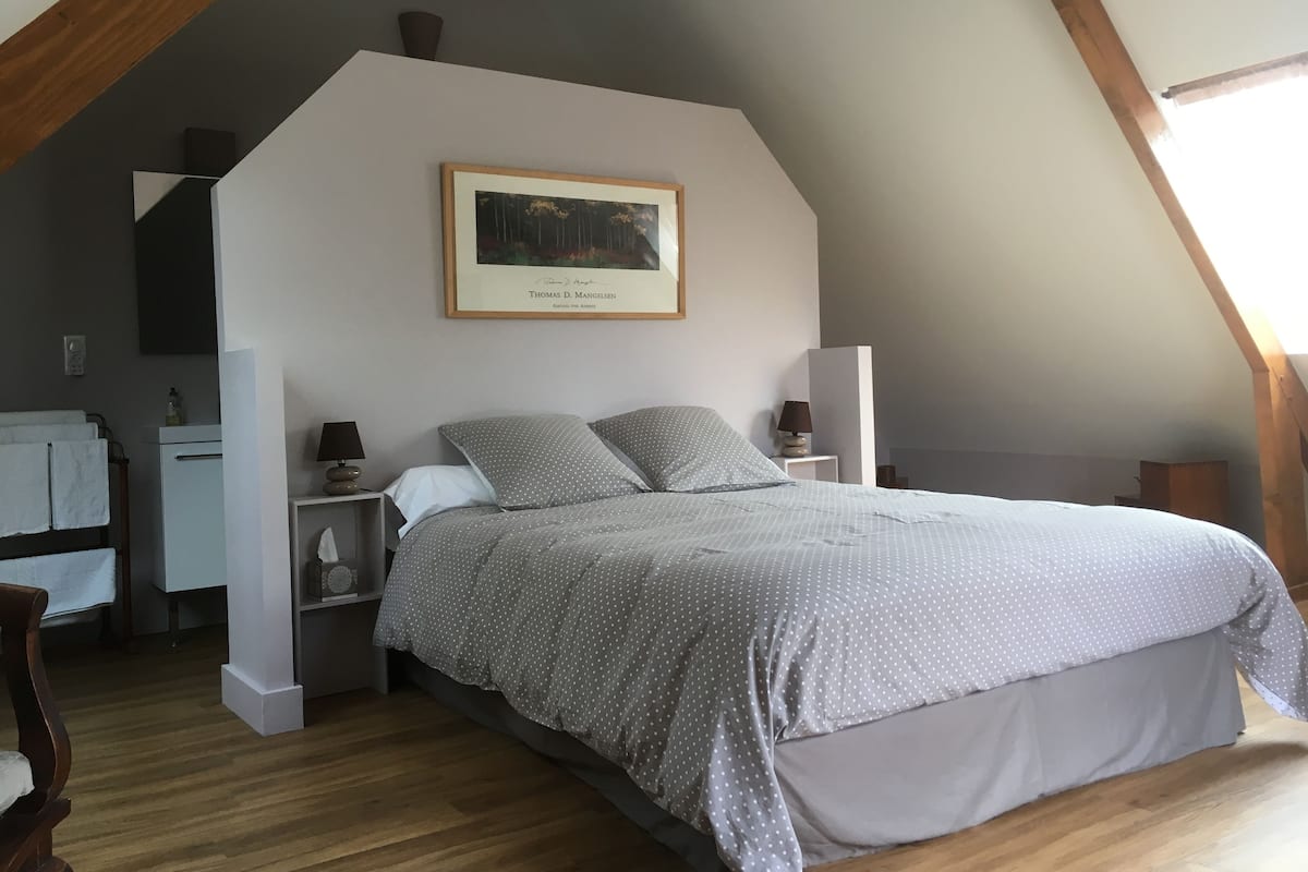 Un dormitorio con una cama, una mesita de noche, una lámpara, un cuadro enmarcado en la pared y un techo de madera.