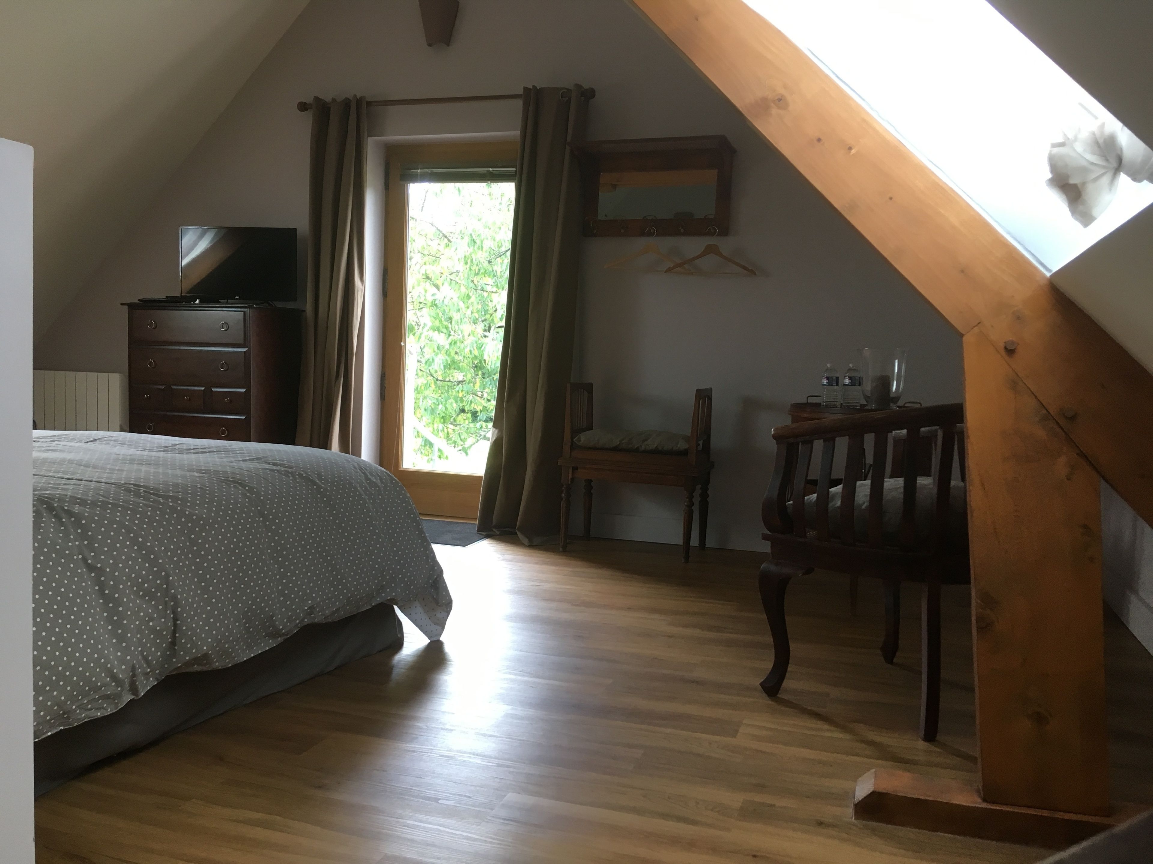 A bedroom with a bed, wooden dresser, chair, and a desk with a mirror.
